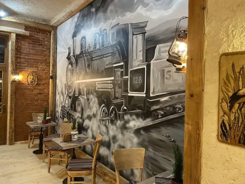Wnętrze restauracji z muralem przedstawiającym lokomotywę i stoliki.