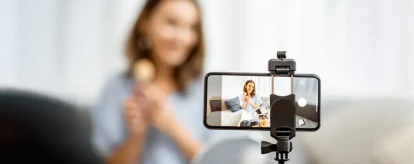 Kobieta nagrywa filmik telefonem komórkowym, trzymając pędzel do makijażu.