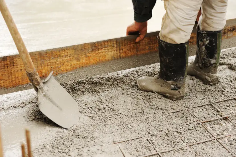 Pracownik w gumowcach układa szalunek do fundamentów. Widać łopatę i świeży beton. Jaki cement na fundamenty?