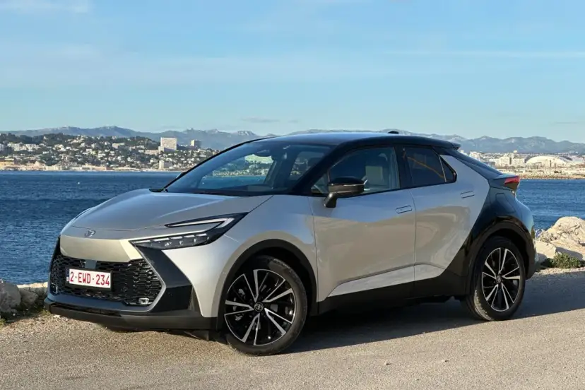 Srebrno-czarna Toyota C-HR na tle morza i miasta. Zastanawiasz się, ile przejedzie hybryda Toyoty na jednym ładowaniu?