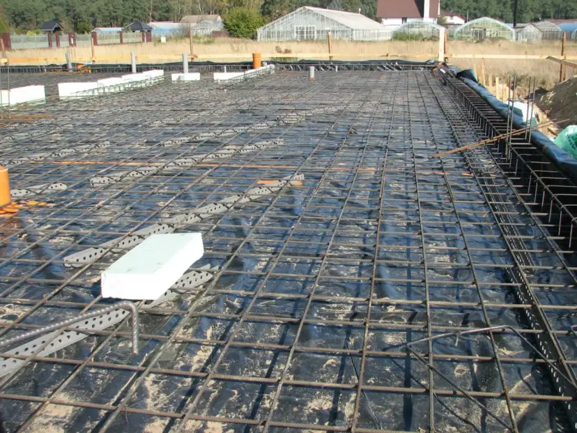 Siatka zbrojeniowa na folii izolacyjnej, przygotowana do wylania betonu. Widać elementy izolacji i rury. To kluczowy etap, by wiedzieć, ile drutu na fundament.