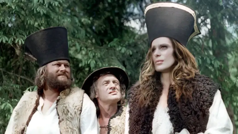 Trzej bohaterowie w strojach z baśni o 12 miesiącach: brodaty mężczyzna, starszy pan i młoda kobieta w futrzanych kamizelkach i wysokich czapkach.