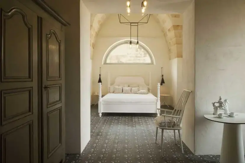 Przytulna sypialnia w stylu hiszpańskim z łóżkiem z baldachimem, kamiennymi łukami i wzorzystą podłogą.