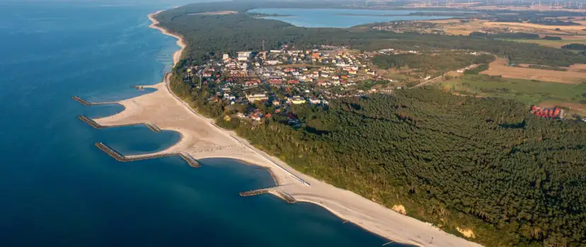 Widok z lotu ptaka na nadmorską miejscowość, gdzie jest Jarosławiec, z piaszczystą plażą, morzem i lasem sosnowym.