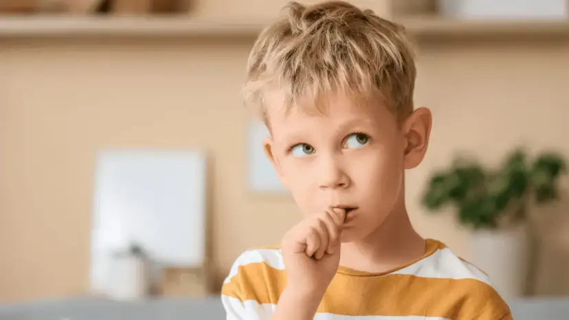 Chłopiec z blond włosami obgryza paznokcie, zastanawiając się, dlaczego dzieci to robią.