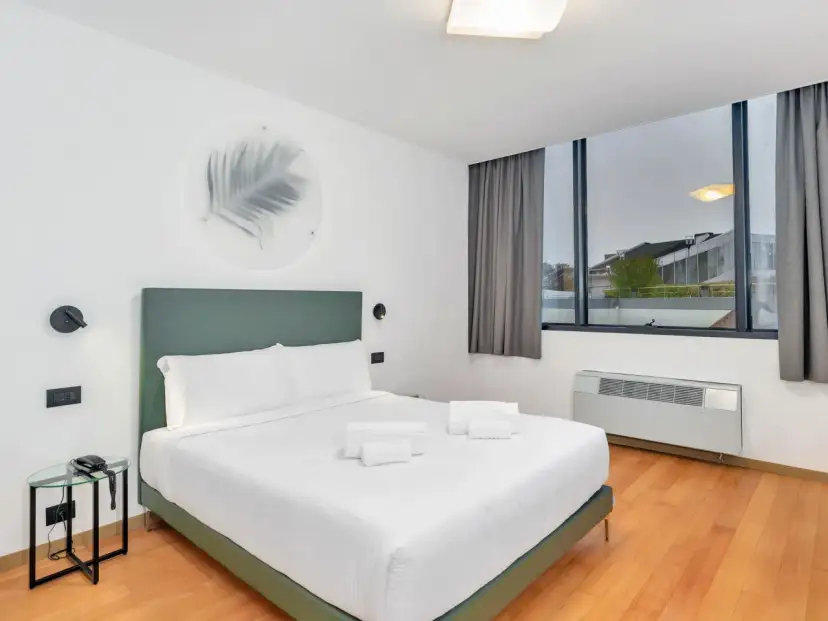 A modern hotel room with a king-size bed, white linens, and a green headboard.