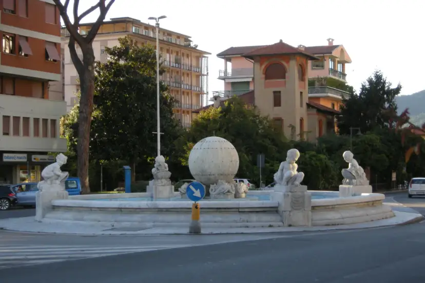 Fontanna z rzeźbami dzieci i kulą w centrum, otoczona budynkami w Marina di Massa.