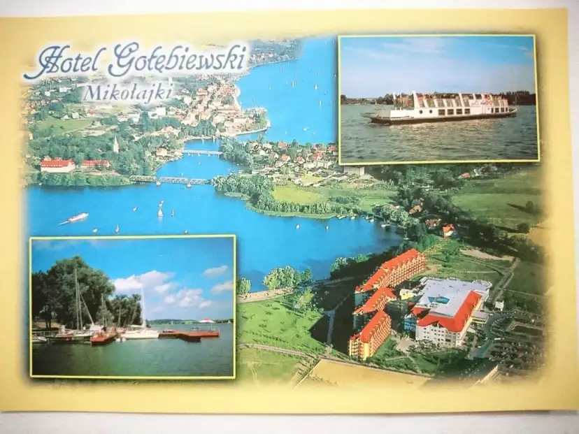 Widok na Hotel Gołębiewski w Mikołajkach i jezioro. Widoczny statek wycieczkowy i żaglówki.