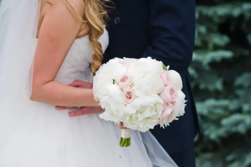 Piękny bukiet ślubny z białych piwonii i różowych frezji, trzymany przez parę młodą.