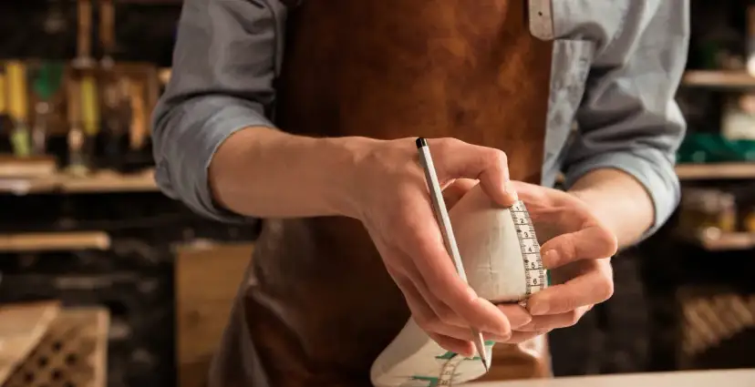 Ręce mierzą długość buta centymetrem i ołówkiem.