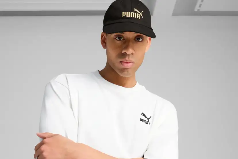 Mężczyzna w czarnej czapce z logo Puma i białej koszulce.