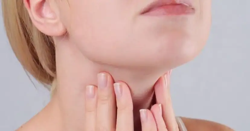 Kobieta dotyka szyi, gdzie znajduje się tarczyca. Wyniki badań wskazują na ft3 podwyższone tsh w normie, co może wymagać dalszej diagnostyki.