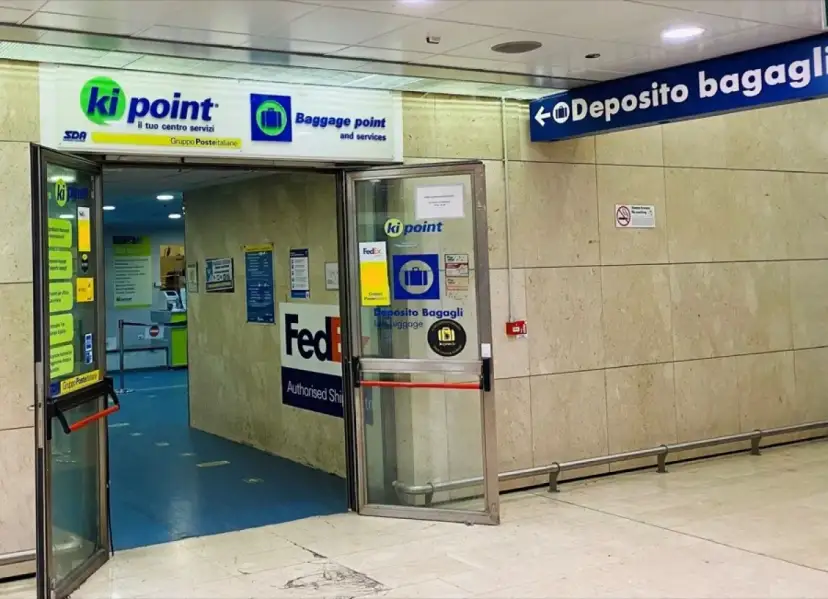 Entrance to a Ki Point baggage storage facility with signage for "Deposito Bagagli" and FedEx.