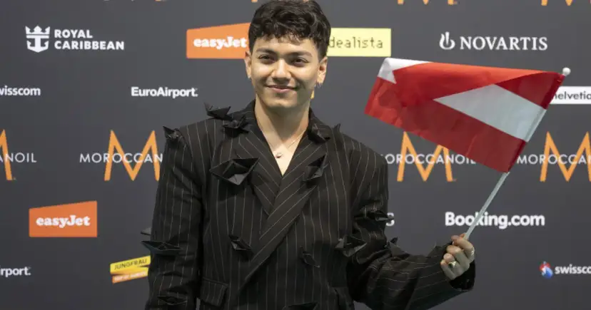 Młody mężczyzna w czarnym garniturze z papierowymi łódkami, trzymający flagę Austrii. Czy to on wygrał finał Eurowizji?