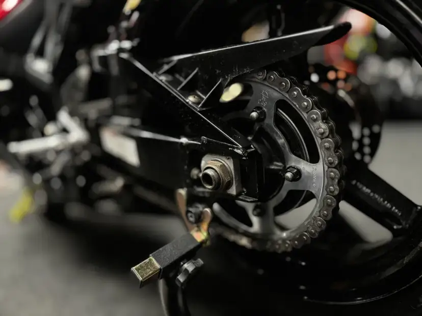Zbliżenie na tylne koło motocykla z widocznym łańcuchem i zębatką. Pokazuje elementy potrzebne do tego, jak rozkuć łańcuch motocyklowy.