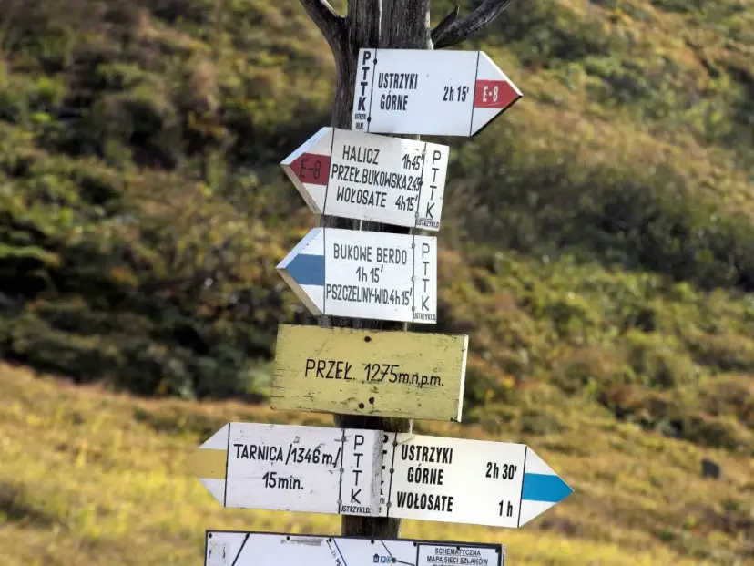 Znaki szlaku turystycznego PTTK. Wskazują kierunki i czas dojścia do różnych miejsc, np. Ustrzyki Górne, Tarnica. Czarny szlak oznacza trasę o średnim stopniu trudności.