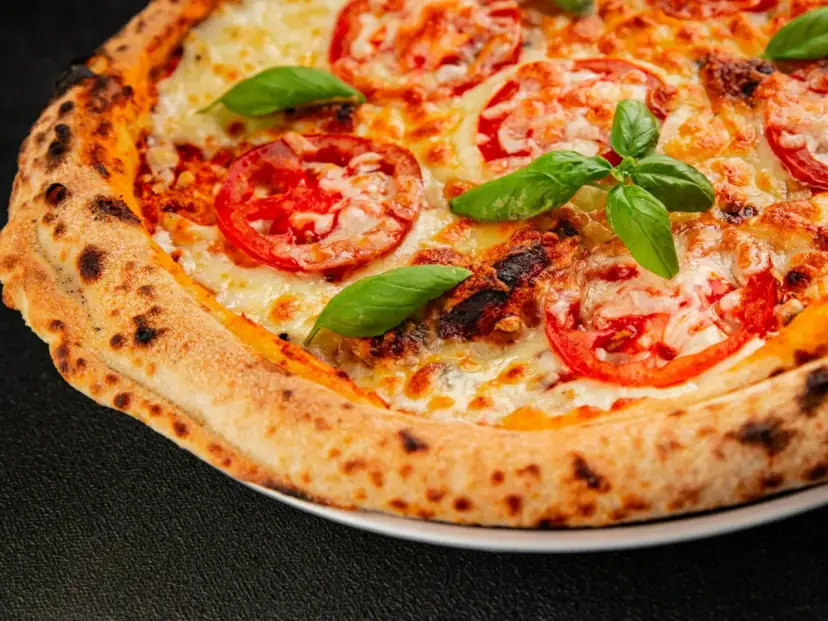 Pyszna pizza Margherita z pomidorami i bazylią, idealnie wypieczona w wysokiej temperaturze przez kilka minut.