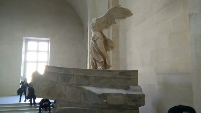 Skrzydlata Nike, symbol zwycięstwa, niczym mit, unosi się nad kamiennym postumentem.