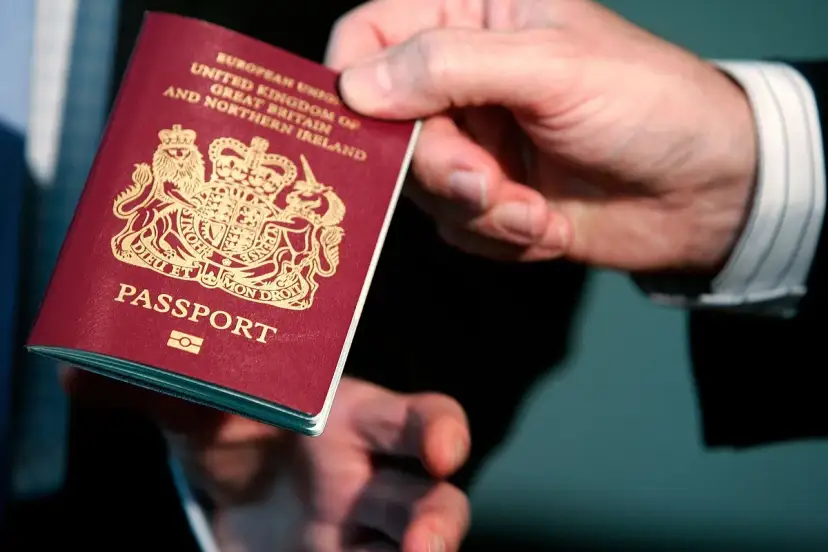 Dłoń podaje paszport biometryczny Wielkiej Brytanii. Widoczny herb i napis "PASSPORT".
