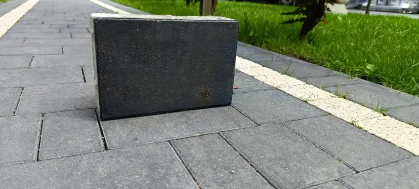 Ciemnoszara kostka na szarym podjeździe z białym pasem i zieloną trawą w tle.