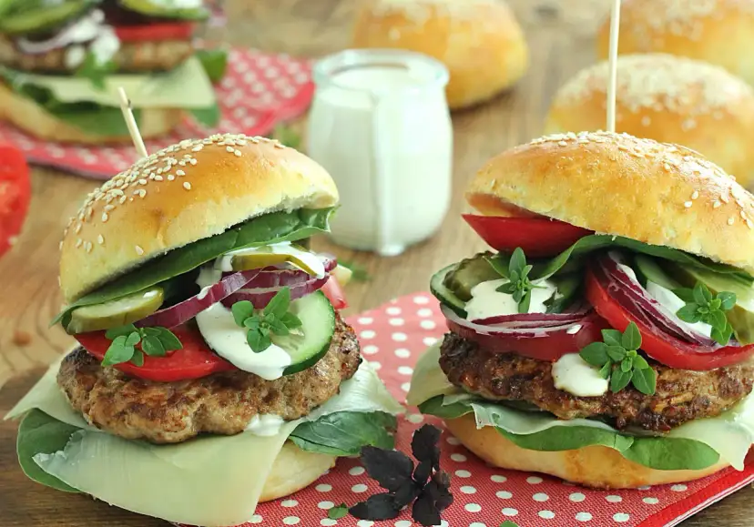 Dwa soczyste burgery wołowe z dodatkami na drewnianym tle.