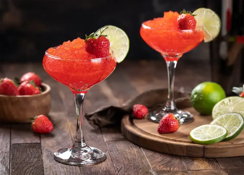 Dwa mrożone daiquiri truskawkowe z limonką i truskawkami, na drewnianym stole.