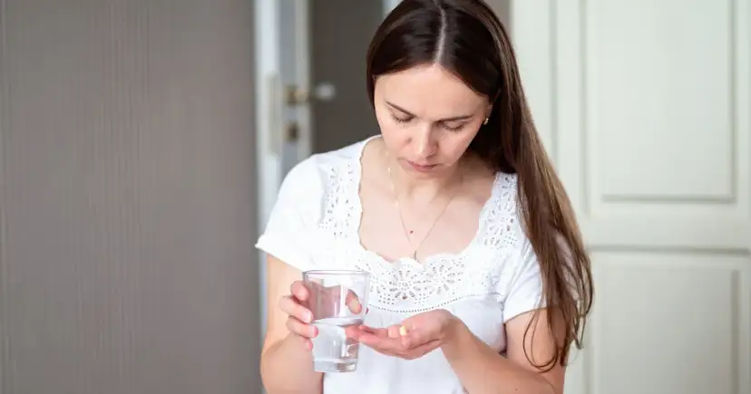 Kobieta trzyma szklankę wody i tabletkę na dłoni.