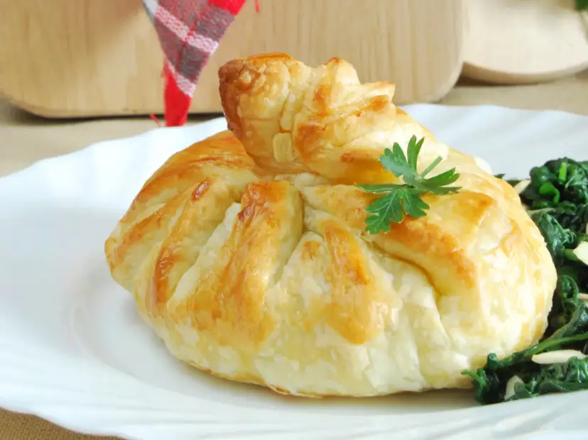 Złociste sakiewki z ciasta francuskiego, ozdobione natką pietruszki, podane z zielonymi warzywami.