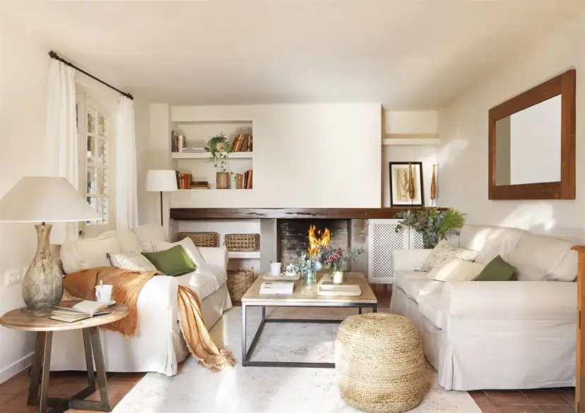 Salón acogedor con chimenea encendida, sofás blancos, mesa de centro de madera y detalles decorativos.