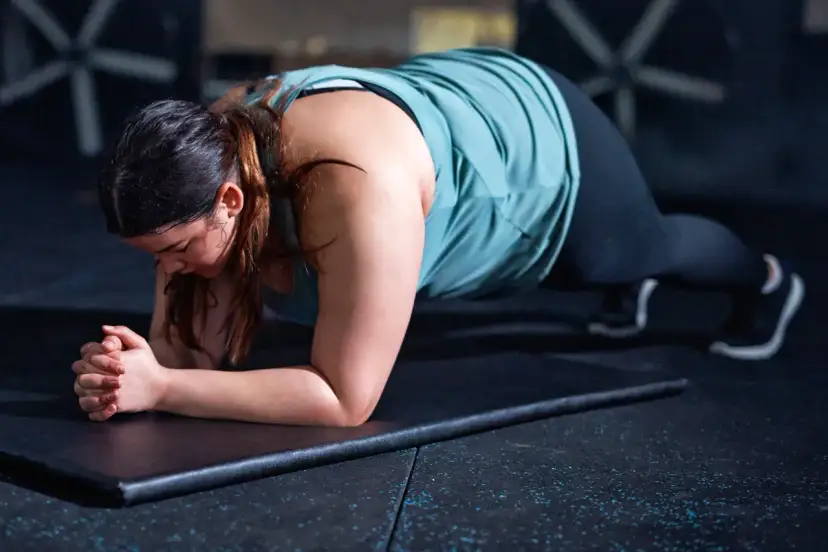Kobieta wykonuje plank, jedno z ćwiczeń na schudnięcie z brzucha, w siłowni.