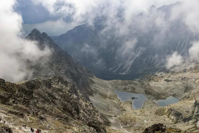 Widok na Tatry z chmurami. Szlak turystyczny prowadzi przez kamieniste zbocza do stawów. Idealne miejsce na **rysy dla początkujących**.