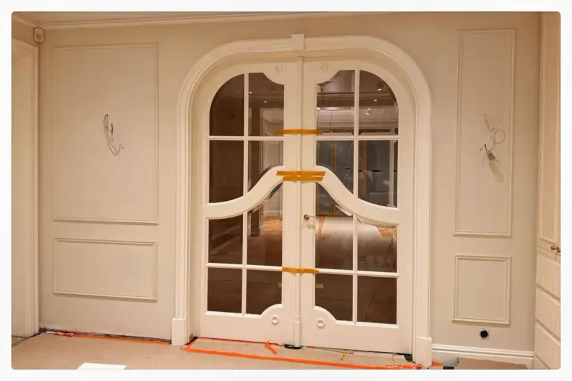 Eleganckie drzwi dwuskrzydłowe z łukiem i panelami ściennymi. Planowanie sztukaterii w tym wnętrzu doda mu klasy.