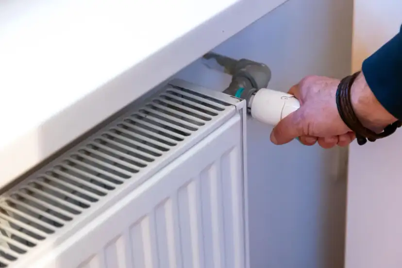Ręka reguluje termostat grzejnika. Dowiedz się, jak wymienić kaloryfer w bloku, by cieszyć się ciepłem.