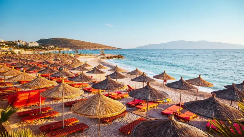 Albania, lipiec: słoneczna plaża z rzędami parasoli i leżaków, turkusowe morze i góry w tle. Idealna pogoda na wakacje.
