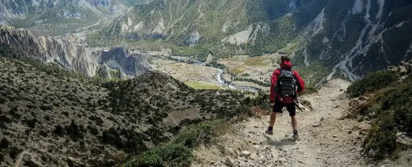 Widok z góry na dolinę i góry. Turysta z plecakiem zastanawia się, co zabrać w góry.