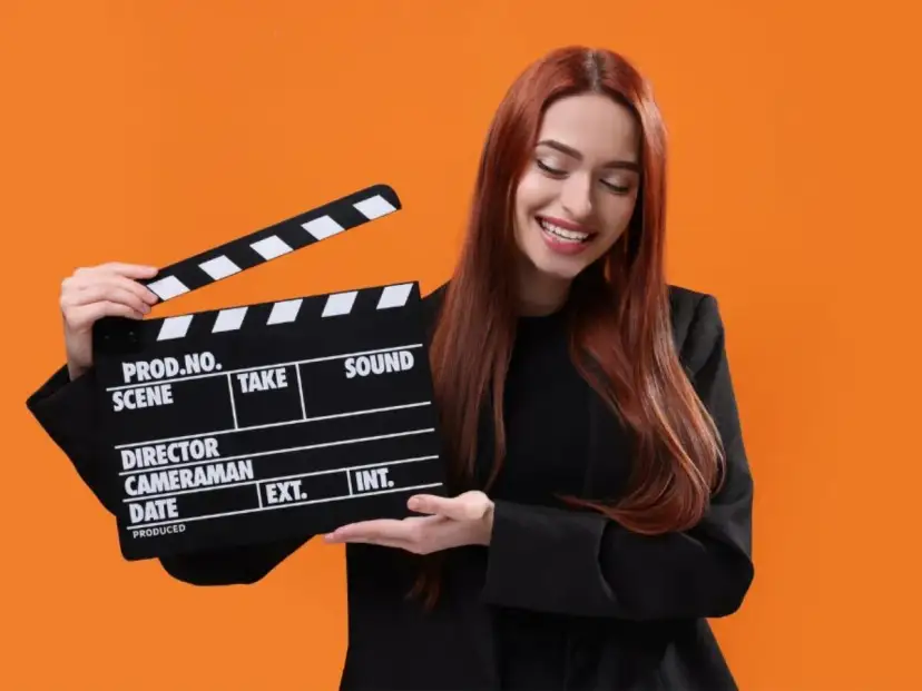 Uśmiechnięta kobieta z rudymi włosami trzyma klaps filmowy. Zastanawiasz się, ile kosztuje hollywood smile w Polsce?