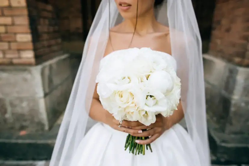 Piwonie na ślub, biały bukiet panny młodej z welonem. Delikatne kwiaty tworzą romantyczną kompozycję.