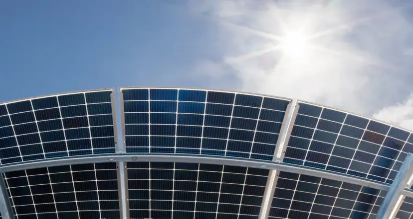 Widok od dołu na zakrzywione panele bifacialne pod błękitnym niebem i słońcem. Mogą pojawić się problemy z montażem, ale to nie są główne wady paneli bifacialnych.