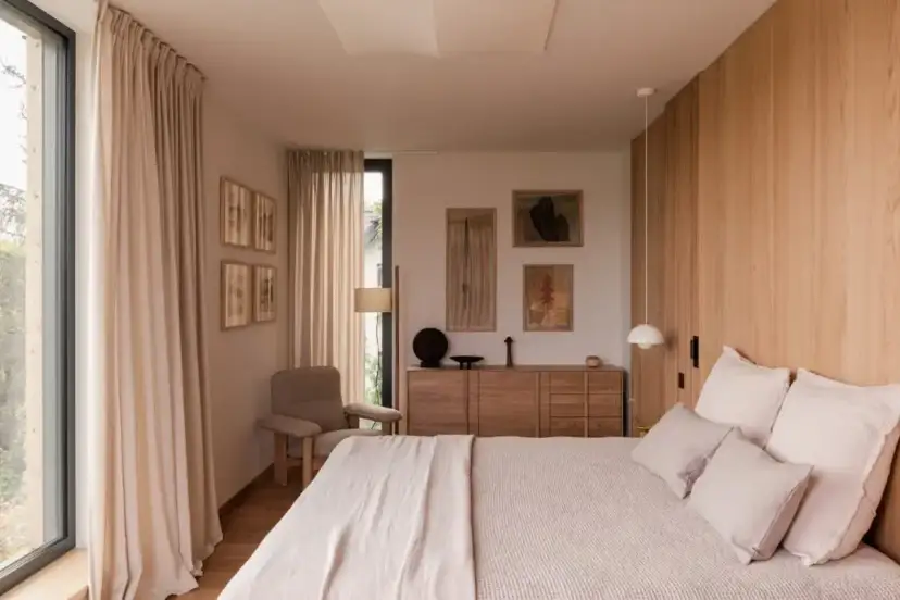 Przytulna sypialnia z łóżkiem, drewnianą komodą, fotelem i obrazami na ścianie.