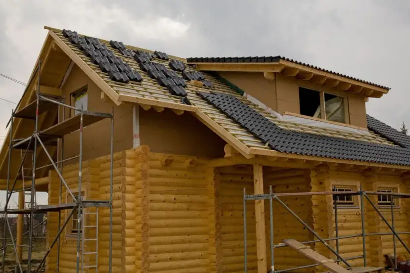 Budowa domu z bali, trwa układanie dachówki. Trudno oszacować ile m3 drewna na dom z bali, ale konstrukcja wygląda solidnie.