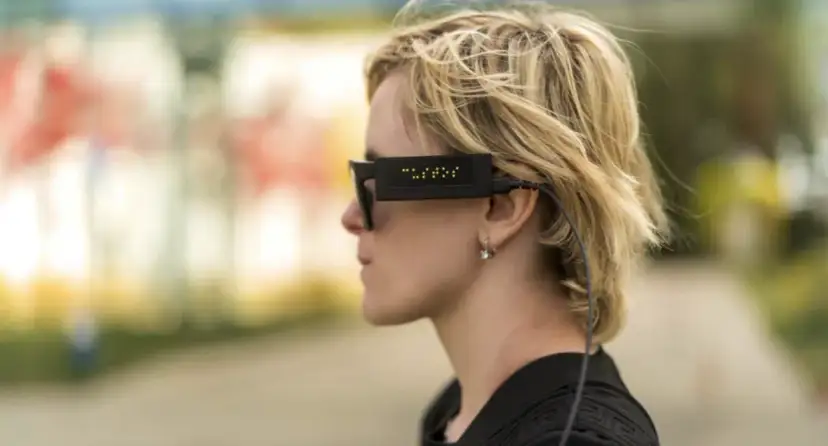 Kobieta w okularach z wyświetlaczem brajlowskim i słuchawką.