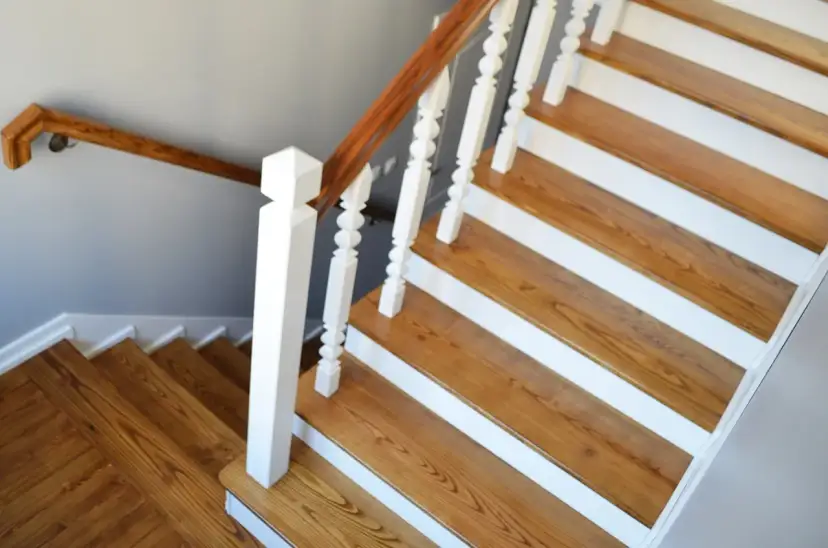 Odnowione drewniane schody z białymi stopniami i brązową poręczą.