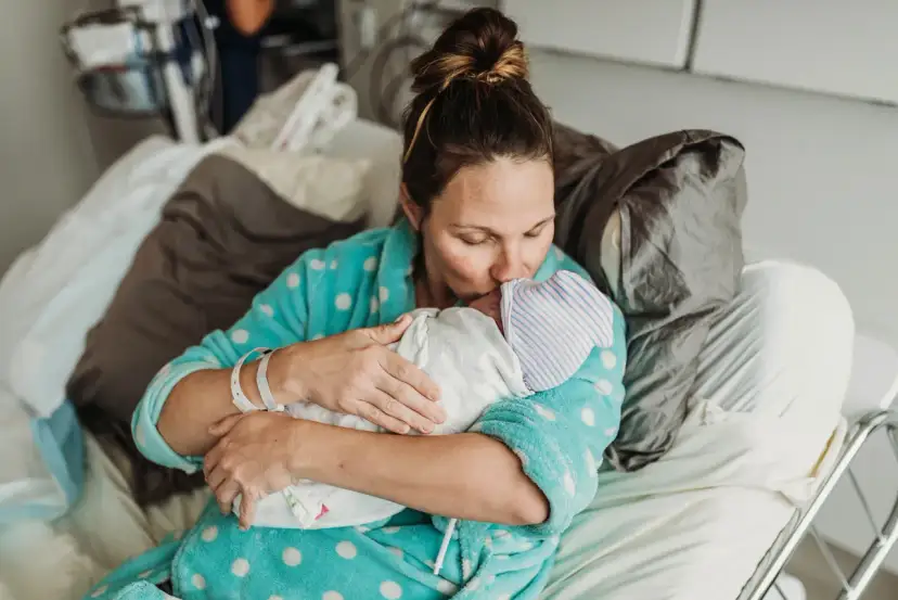 Mama tuli dziecko po cesarce, czule całując je w czapeczkę. Laktacja po cesarce może być wyzwaniem, ale miłość jest silniejsza.