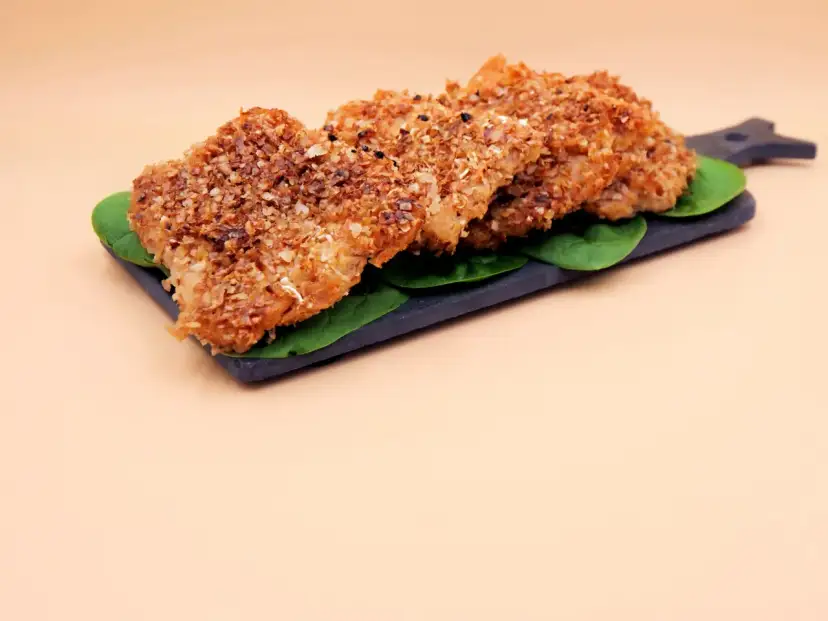 Kotlety sojowe w panierce z płatków na ciemnej desce z liśćmi szpinaku.