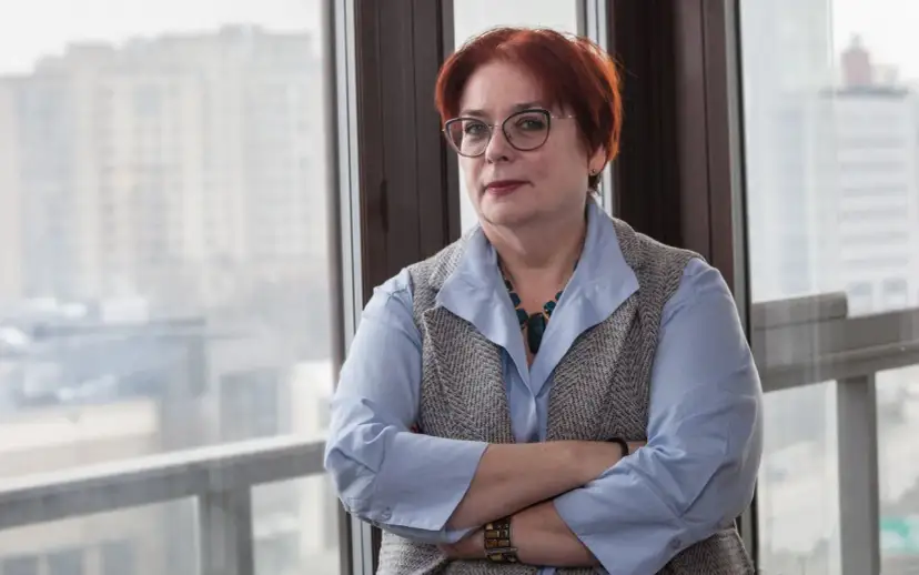 Kobieta w okularach, z rudymi włosami, opiera się o okno. Jej postawa sugeruje siłę i determinację w odpowiedzi na pytanie, jak żyć po rozwodzie.