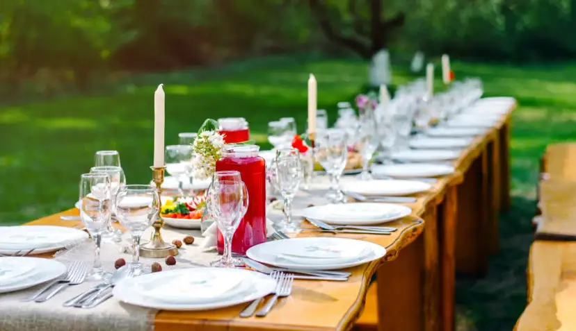 Piękne przyjęcie w ogrodzie. Długi stół nakryty do kolacji, z kieliszkami, talerzami i świecami.