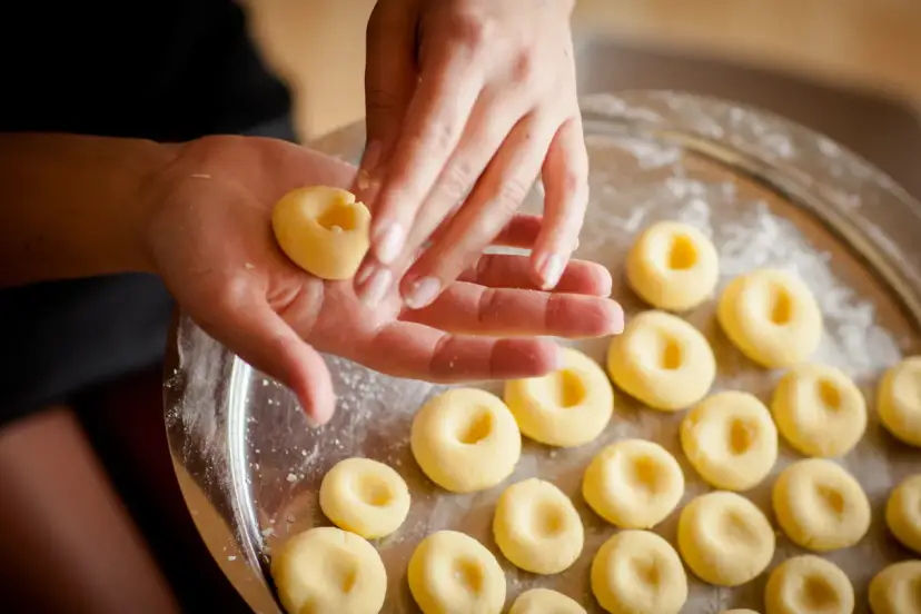Dłonie formują kluski śląskie z ciasta na tacy.