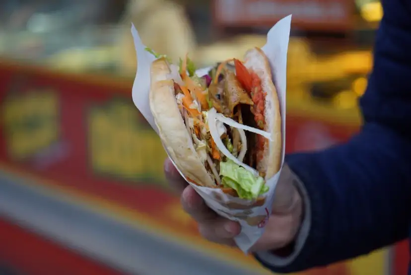 Kebab w bułce z warzywami i mięsem, trzymany w dłoni.