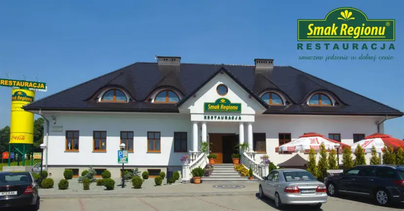 Restauracja "Smak Regionu" z białym budynkiem, schodami i samochodami na parkingu.