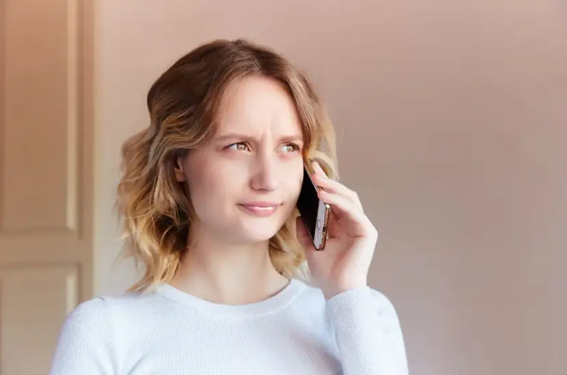 Zmarszczona kobieta rozmawia przez telefon, próbując dowiedzieć się, jak zwiększyć głośność w telefonie, bo rozmówca mówi za cicho.